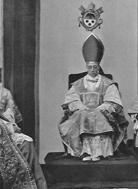 Papst Pius XII. sitzt in seinen päpstlichen Gewändern auf seinem Papststuhl.
