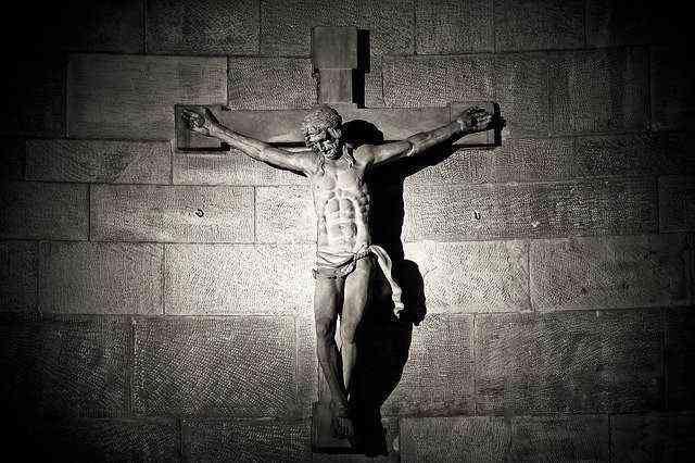 An einer grauen dunklen Mauerwand hängt ein Kruzifix: Jesus Christus hängt am Kreuz in erschütternder Weise