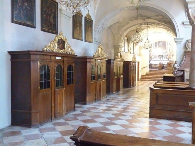 Nach der Erforschung des Gewissens empfängt man das Sakrament der Buße: ein langer Gang in einer barocken Kirche, in der auf der linken Seite aus Holz erbaute schöne und einladende Beichtkabinen stehen, um die Sünden zu Beichten und die Lossprechung zu erhalten