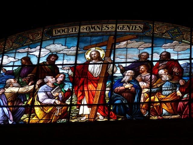 Ein Fensterbild, in dem Christus den Aposteln den Missionsauftrag gibt: Lehret alle Völker; Jesus hält sein Kreuz in der einen Hand; die Apostel schauen Ihn anbetend an