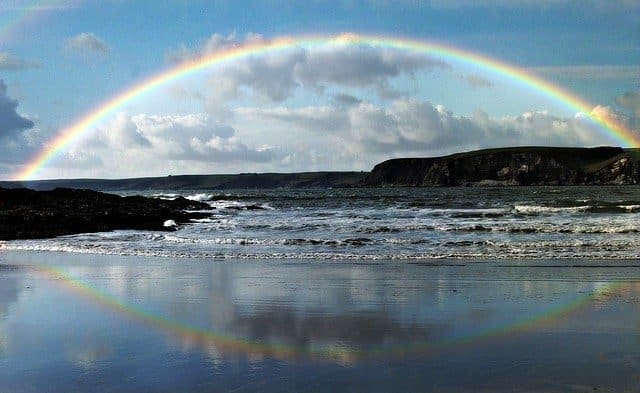 Der Regenbogen als Zeichen des Bundes Gottes mit Noe; der Regenbogen am Strand des Meeres als Halbkreis spiegelt sich im Wasser und wird dadurch zu einem vollen Kreis