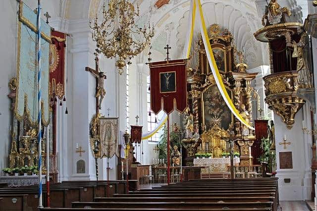 Das Kirchenjahr in seinen Festen: die Kirche ist geschmückt nicht nur mit dem barocken Hochaltar, Seitenaltar, Kanzel und Statuen, sondern auch mit einem weiß-gelben, von der Decke zu beiden Seiten hin herab fallenden Band und zweier Prozessionsfahnen im Vordergrund