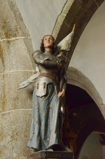 Eine Statue der Heiligen Johanna von Orleans in Rüstung und mit Fahne, die Augen zum Himmel gerichtet